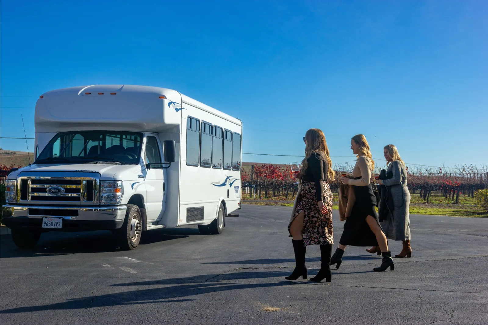 Small tour shuttle bus with guests walking toward it near a Napa Valley vineyard